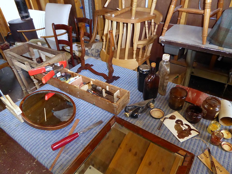French polishing work in progress: jars of polish, rubbers, a scraper and a small round mirror frame on the bench